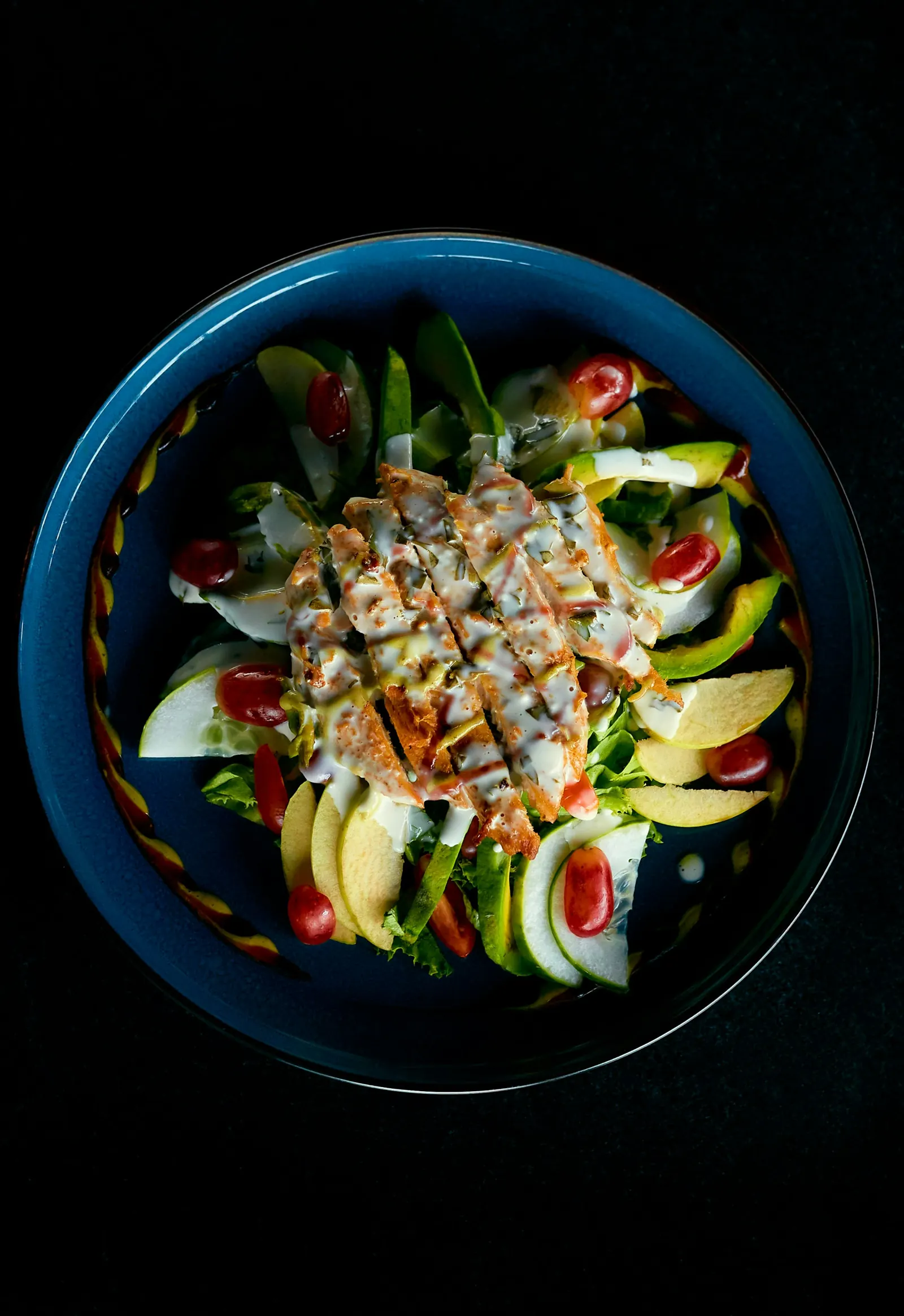 Grilled chicken salad with avocado, egg and tomatoes on a dark plate