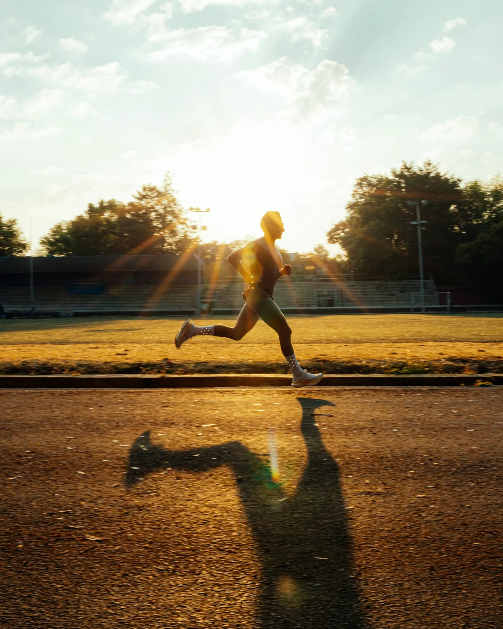 Runner sprinting down a track into low golden sunlight