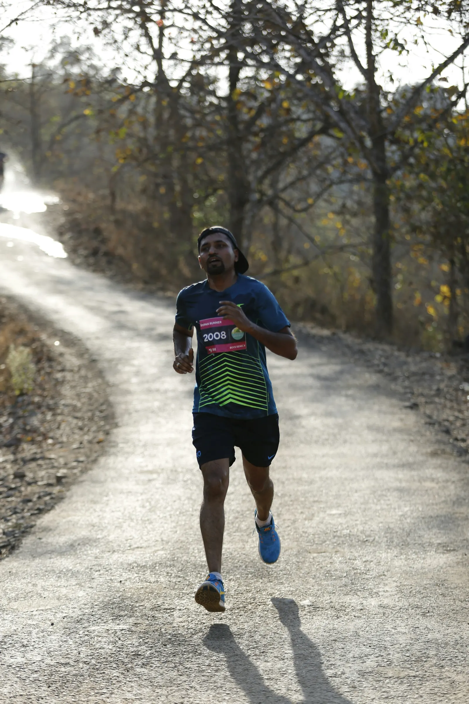 Indian runner with a race bib climbing a forest road